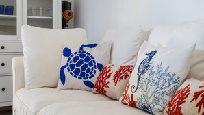 Un sofá blanco con tres almohadones decorativos que muestran una tortuga, coral rojo y un diseño de caballito de mar.