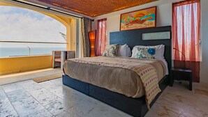 A spacious bedroom with a large bed, a view of the sea, and a ceiling fan.