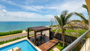 A pool area with a wooden deck, lounge chairs, and a pergola overlooking the ocean.