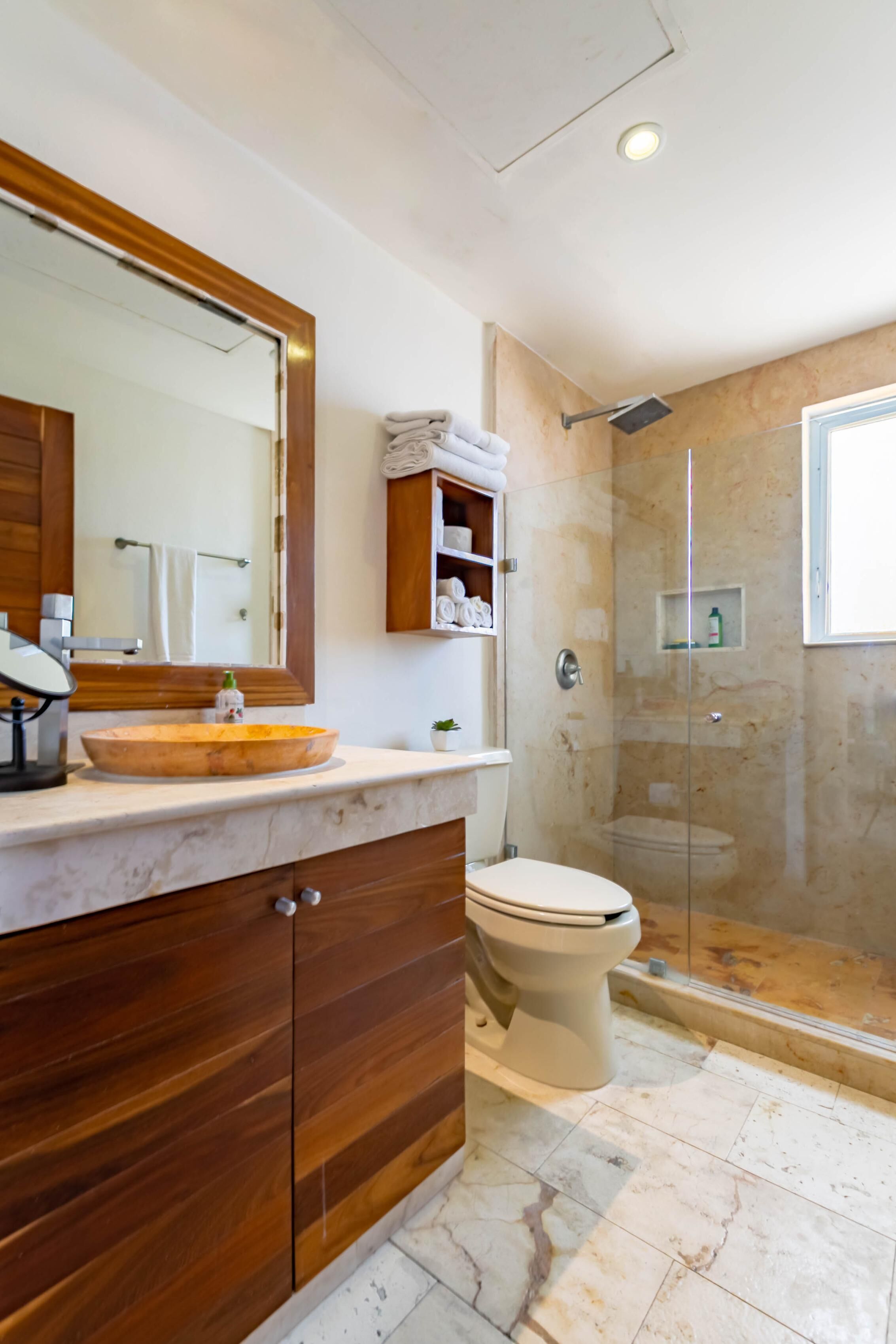 Un baño con tocador de madera, un espejo grande, inodoro y cabina de ducha con paredes de vidrio.