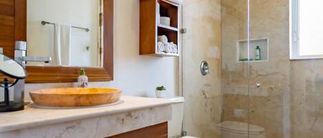 Une salle de bain avec un meuble-lavabo en bois, un grand miroir, des toilettes et une douche séparée par une paroi de verre.
