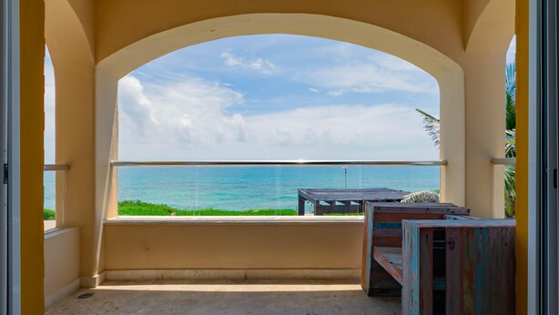 A balcony with a view of the ocean, a wooden table, and a bench.