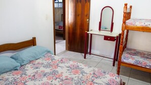 Een slaapkamer met een bed, een houten dressoir met spiegel en een stapelbed.