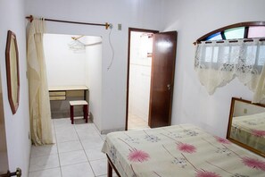 Une chambre à coucher avec un lit, un bureau et une chaise. Une porte donne accès à une autre pièce.