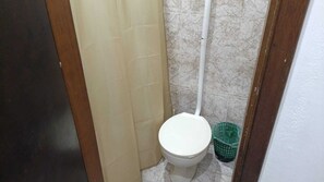 Une petite salle de bain avec des toilettes, un rideau de douche et une poubelle verte.