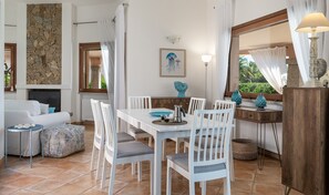 A dining area with white chairs, a table, and a coffee pot. There is a stone wall and a painting on the wall. - Villa 'Sofia' with Private Pool, Wi-Fi and Air Conditioning (Costa Rei)