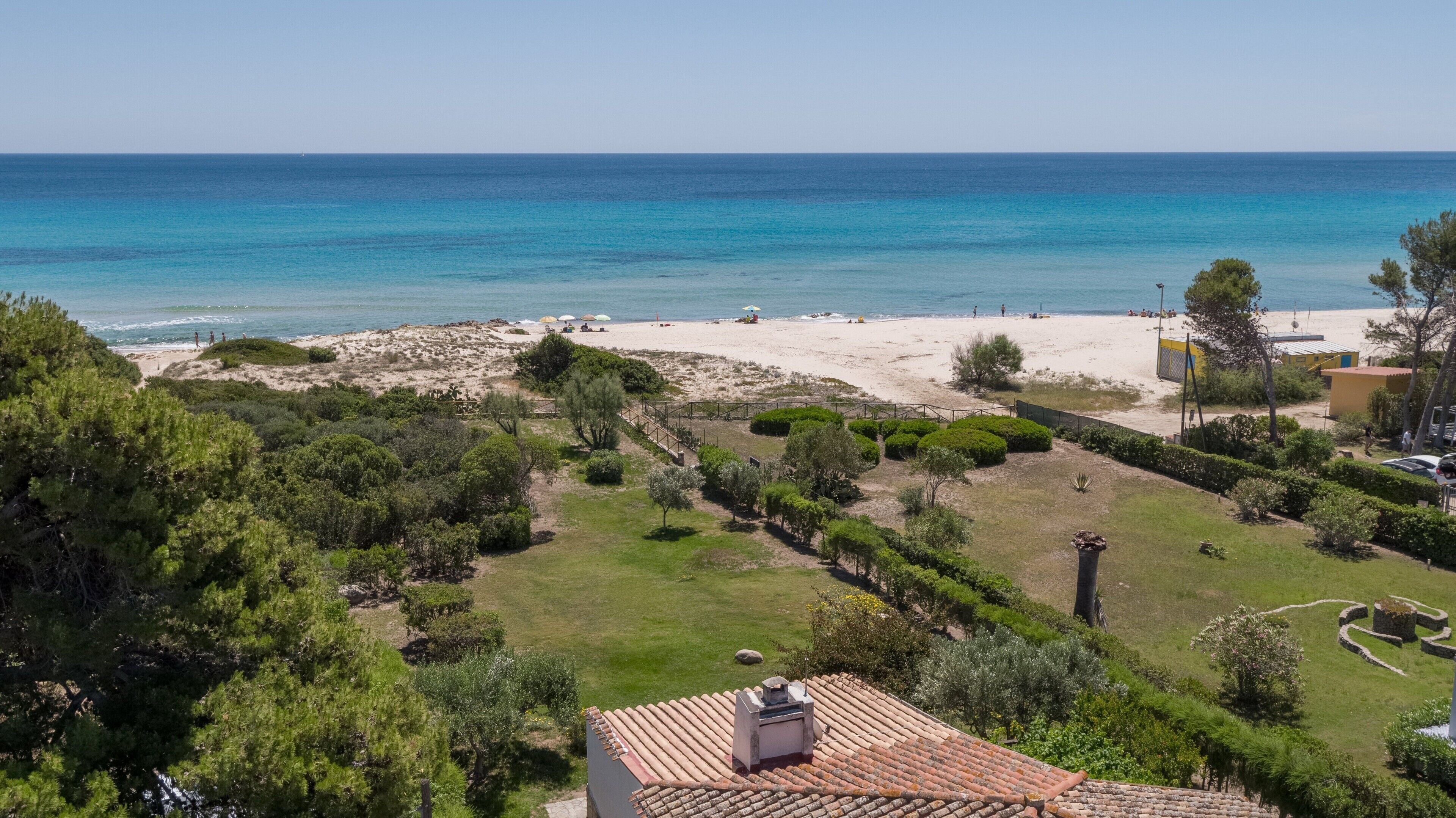 A coastal property with a beach, green lawns, and a tiled roof.