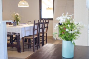 A dining area with a table set for four, wooden chairs, a vase with flowers, and a hanging light fixture.