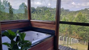 A hot tub in a wooden cabin with a view of a forested landscape. - Chalés Luz do Luar (Campos do Jordao)