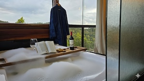 A room with a bathtub filled with bubbles, a book, a wine bottle, and a glass on a wooden tray. - Chalés Luz do Luar (Campos do Jordao)