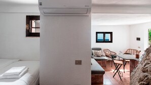 Una stanza con un letto, una finestra, un condizionatore d'aria a muro e un angolo salotto con sedie e un tavolo.
