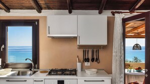 A kitchen with a view of the sea, a gas stove, a sink, and hanging kitchen utensils. - Villa 'Nido 3' with Sea View, Wi-Fi and Air Conditioning (Costa Rei)