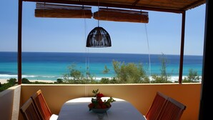 A balcony with a table, chairs, a hanging light fixture, and a view of the ocean. - Villa 'Nido 3' with Sea View, Wi-Fi and Air Conditioning (Costa Rei)