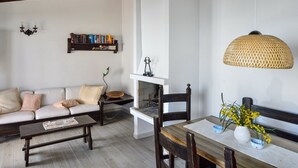 A living room with a sofa, coffee table, and a dining table with chairs. There is a bookshelf with books and a wall-mounted lamp. - Villa 'Nido 3' with Sea View, Wi-Fi and Air Conditioning (Costa Rei)