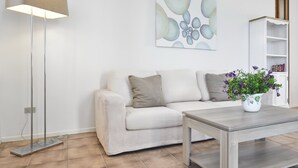 A living room with a sofa, a coffee table, a floor lamp, a painting, and a bookshelf. - Villa 'Massidda' with Sea View, Wi-Fi, and Air Conditioning (S.Margherita di Pula)