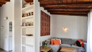 A living room with a grey sofa, a wooden coffee table, a clear glass chair, a bookshelf, and a patterned wall hanging. - Villa 'Villetta 9' with Private Terrace, Wi-Fi and Air Conditioning (Costa Rei)