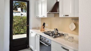 A kitchen with white cabinets, a stove, and a view through a door. - Villa 'Villetta 9' with Private Terrace, Wi-Fi and Air Conditioning (Costa Rei)