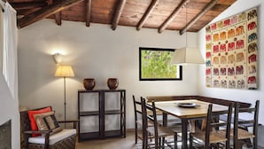 A dining area with a wooden table and chairs, a lamp, a sofa with cushions, and a wall with a colorful tapestry. - Villa 'Villetta 9' with Private Terrace, Wi-Fi and Air Conditioning (Costa Rei)