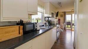 La cuisine est équipée d’un four à micro-ondes, d’un grille-pain et d’une boîte à pain en bois. Une fenêtre offre une vue sur l’extérieur.