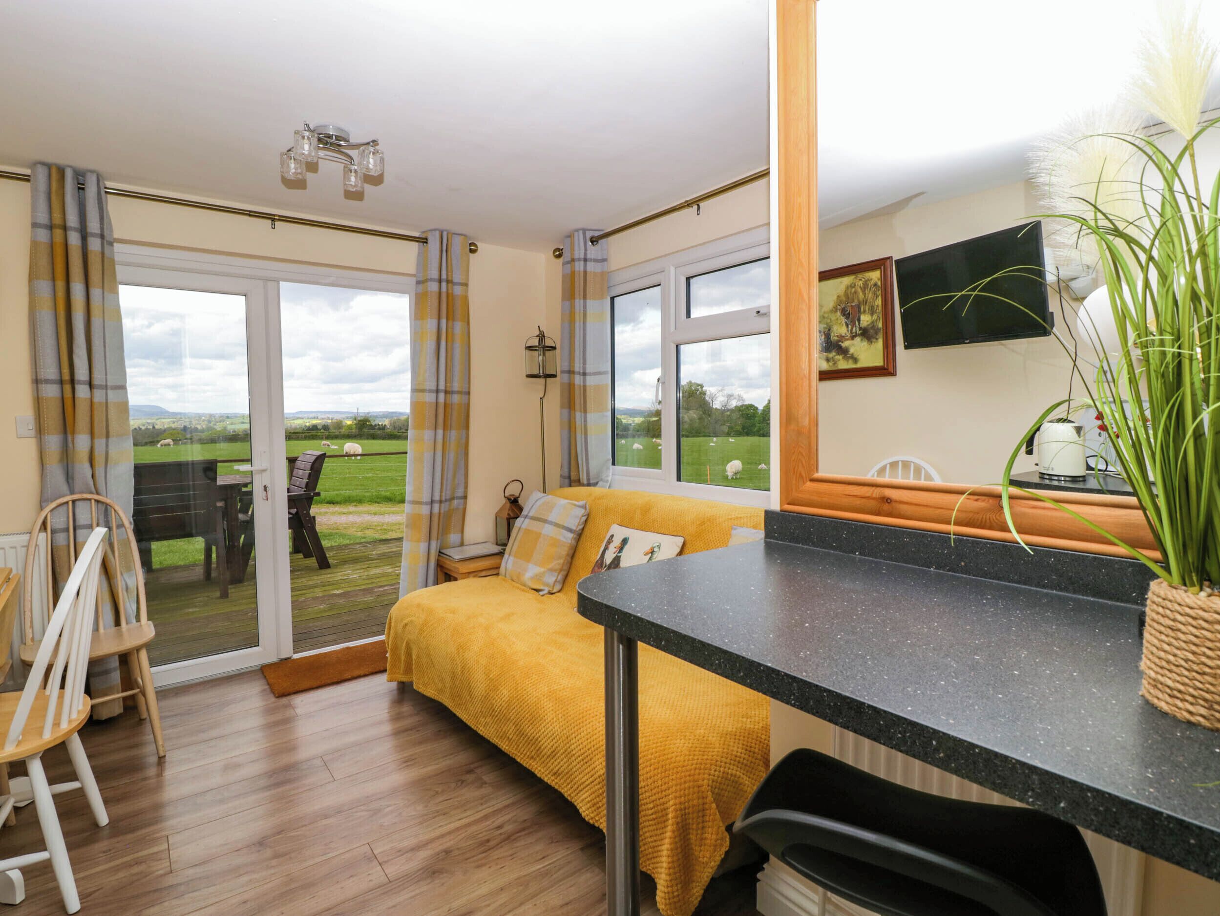 A cozy room with a sofa, a dining table, and a view of a green field with sheep.