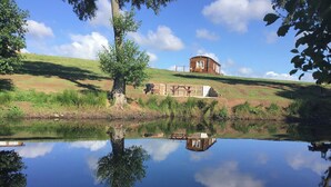 Une cabane en bois située sur une colline, dont le reflet se dessine clairement sur la surface calme d’un plan d’eau.