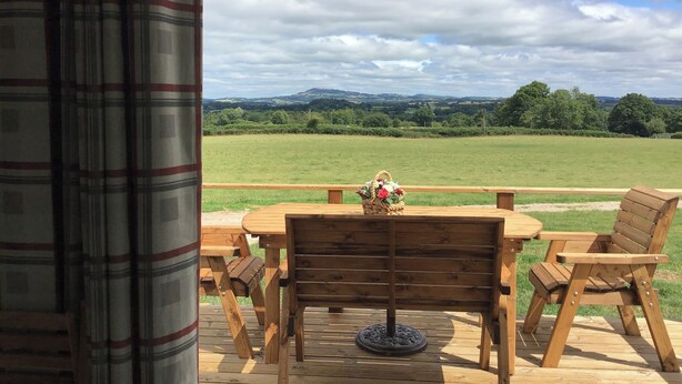Une terrasse en bois avec une table et des chaises, donnant sur un champ verdoyant et des collines.