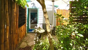 Un jardin avec un arbre, une clôture en bambou et un chemin de pierres menant à une porte.