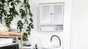 Een moderne badkamer met een witte wastafel, houten kastjes, een magnetron en een zacht tapijt.