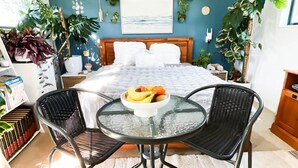 Een slaapkamer met een bed, een glazen tafel met fruit, twee stoelen en verschillende planten.