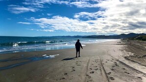 Iemand staat op een zandstrand, met voetafdrukken die naar de oceaan leiden, onder een gedeeltelijk bewolkte lucht.