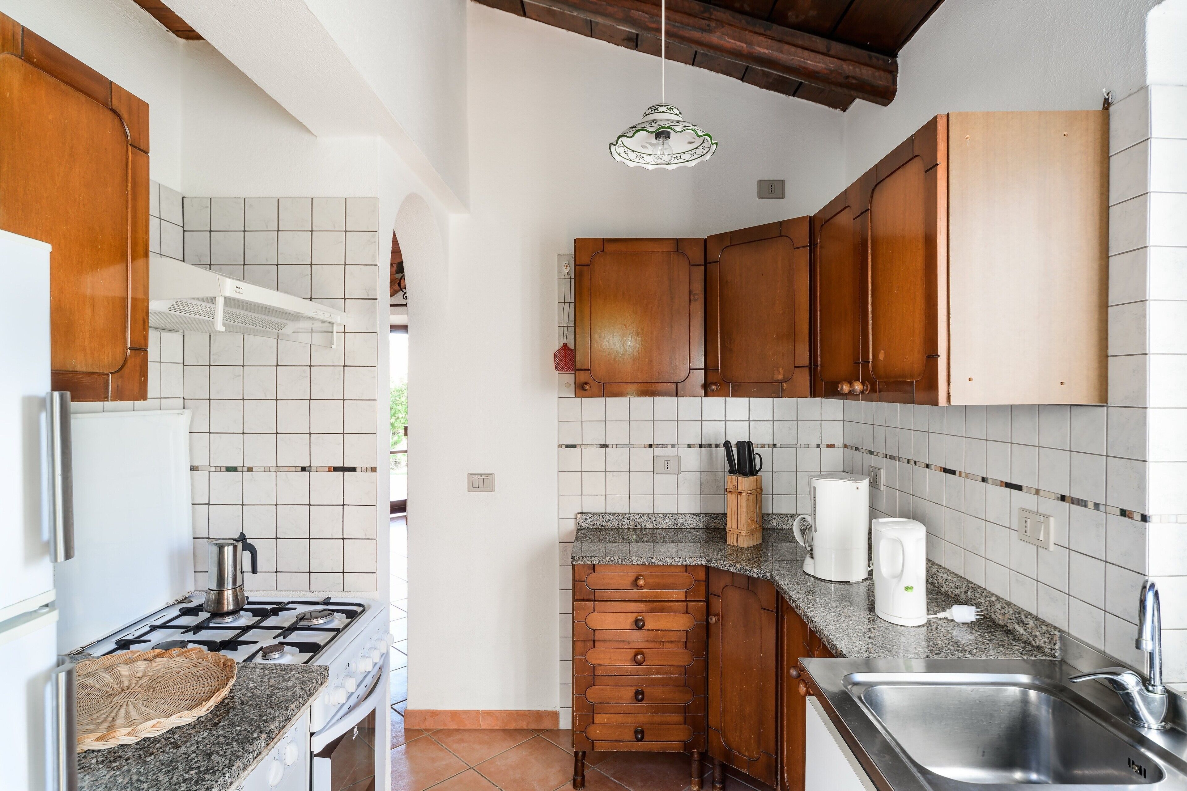 Une cuisine compacte équipée d’une cuisinière à gaz, de meubles en bois, d’un évier et d’un plan de travail sur lequel se trouvent une machine à café et des ustensiles.