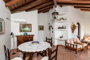 A dining area with a round table, chairs, a ceiling fan, and a wall-mounted shelf with decorative items.