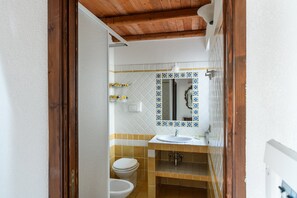 A bathroom with a wooden ceiling, a white toilet, a sink, and a mirror with a decorative tile backsplash.