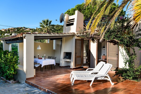 A patio with a table and chairs, a grill, and lounge chairs.