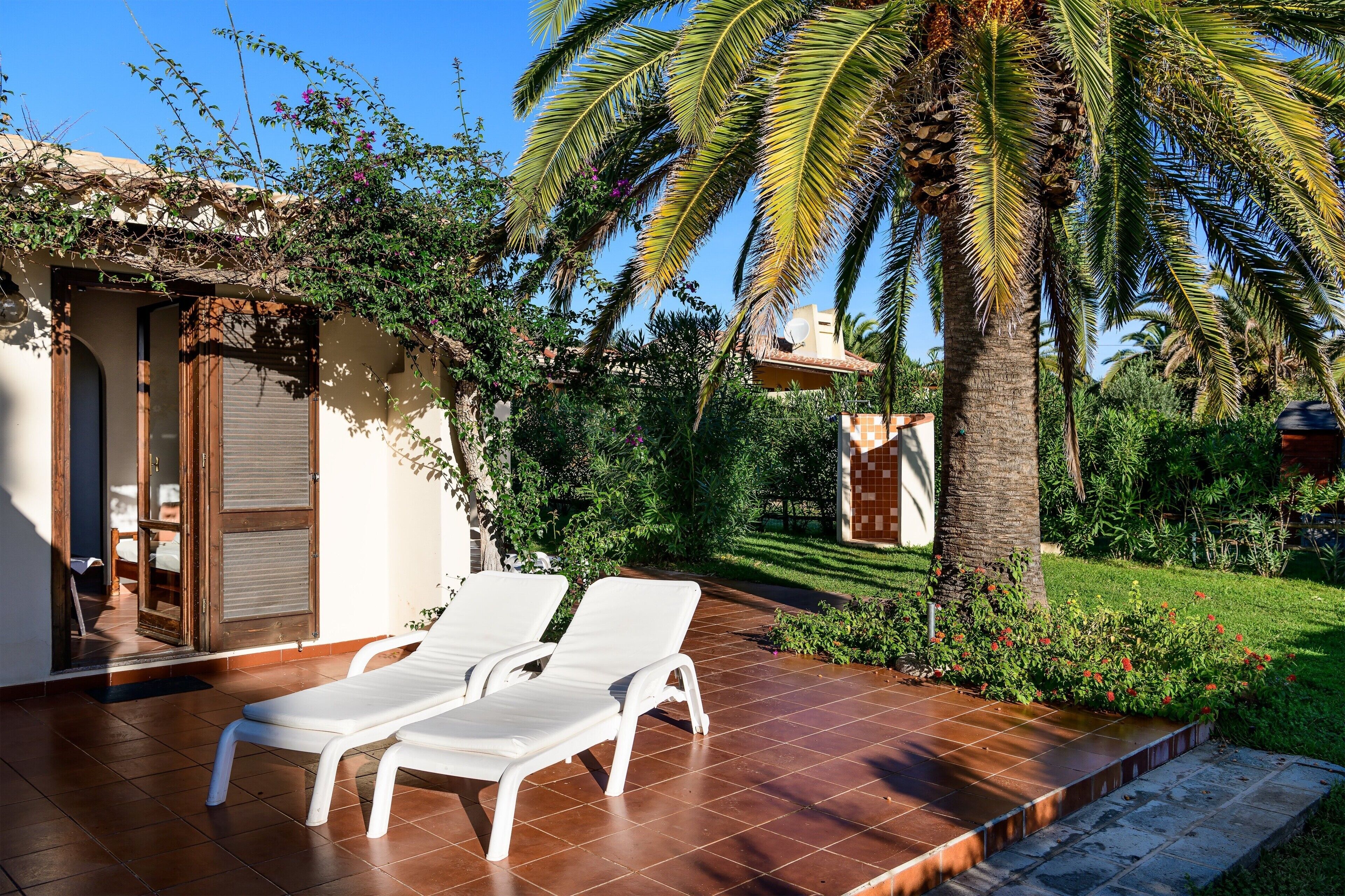 Un patio con dos sillones blancos, una palmera y un jardín cuidado.