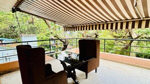 An outdoor seating area with a table and chairs, a striped awning, and a view of greenery.