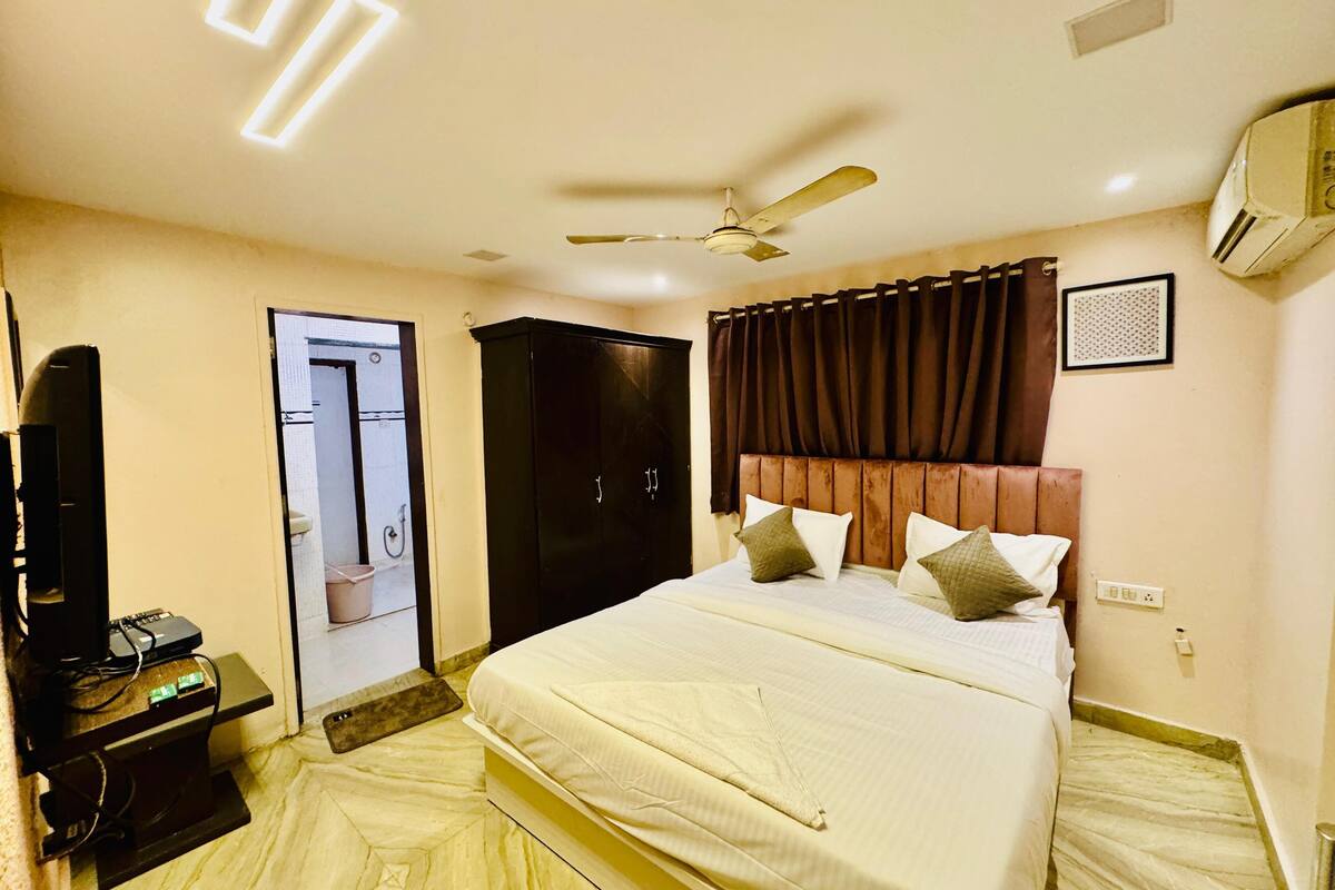 Una habitación de hotel con cama, ventilador de techo, unidad de aire acondicionado, armario y televisor.