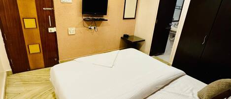 Une chambre d’hôtel avec un lit, un ventilateur de plafond, un téléviseur fixé au mur et une porte dotée d’un miroir.