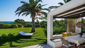 A patio with a lounge chair, a table with a patterned tablecloth, and a view of the sea. - Villa 'Villetta 3' with Sea View, Wi-Fi and Air Conditioning (Costa Rei)