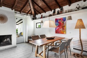 A dining area with a wooden table, wicker chairs, a fireplace, and a colorful abstract painting.