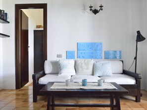 A living room with a sofa, a coffee table, a wall-mounted light fixture, and a door leading to another room.