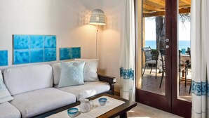 Une pièce avec un canapé, une lampe, une table avec des tasses et une vue sur la mer par une porte.