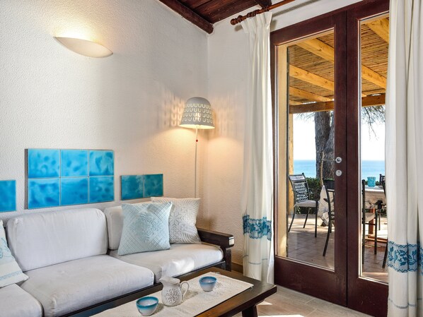 A room with a sofa, a lamp, a table with cups, and a view of the sea through a door.