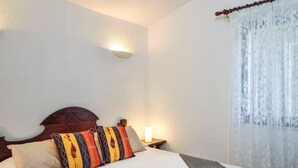 Une chambre à coucher avec un lit, des oreillers, une lampe de chevet et une fenêtre avec un rideau.