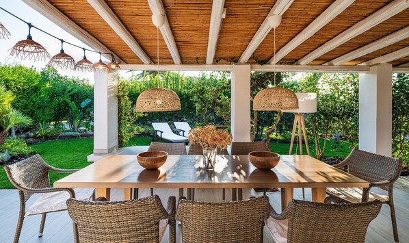 An outdoor patio with a wooden table, wicker chairs, and hanging lights.