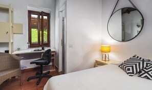 Ein Schlafzimmer mit Bett, Schreibtisch, Stuhl, Lampe, Spiegel und einem Fenster mit Jalousien.