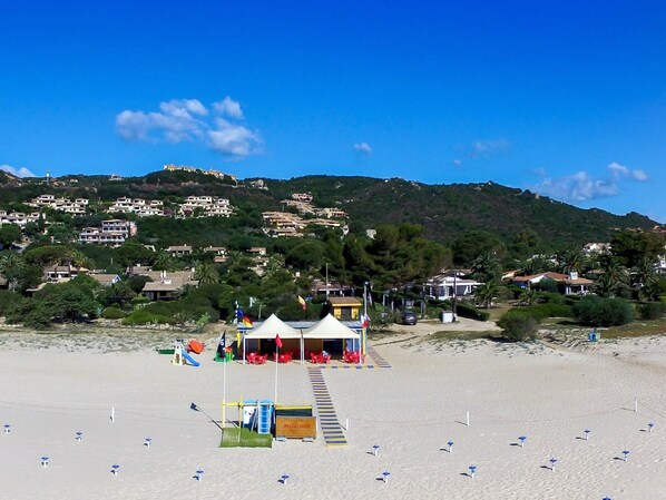 A beach with a lifeguard tower, umbrellas, and a building with a red roof.