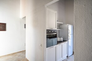 Une cuisine étroite avec des meubles blancs, un four encastré et un réfrigérateur.