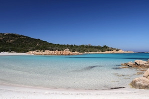 Ein Strand mit klarem türkisblauem Wasser, weißem Sand und Felsformationen.