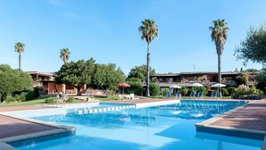 A swimming pool with lounge chairs and umbrellas, surrounded by palm trees and a building with a stone facade. - Villa 'Porto Rotondo' with Sea View, Wi-Fi and Air Conditioning (Porto Rotondo)